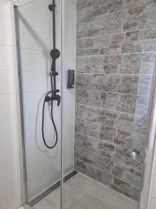 a shower with a glass door and a stone wall at Leander Apartman in Gyömrő