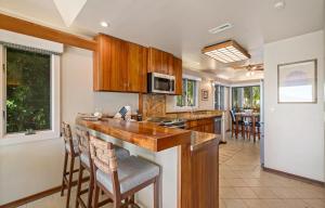 a kitchen with wooden cabinets and a bar with bar stools at Puunoa Beach Estate in Lahaina +25 photos