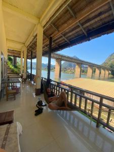 a woman laying in a hammock on a porch with a bridge in the background at Dormitory Hostel Cam Uo in Nongkhiaw
