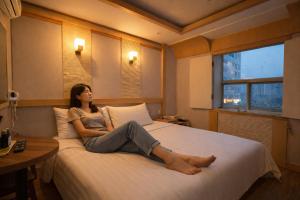a woman sitting on a bed in a hotel room at 평촌코아 in Mabun-ni