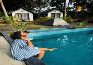 a woman sitting on the edge of a swimming pool at The Wildcamp - Coorg in Kushālnagar