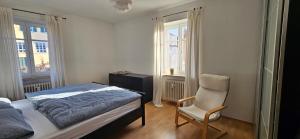 a bedroom with a bed and a chair and two windows at Ferienwohnung Lucia Amorbach in Amorbach