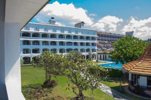 a large white building with a tree in front of it at Hotel Lanka Super Corals in Hikkaduwa