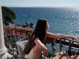 a woman sitting on a balcony looking out at the ocean at Amadria Park Hotel Milenij in Opatija