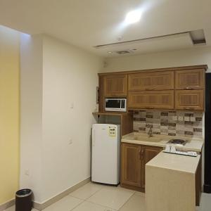 a kitchen with a white refrigerator and wooden cabinets at شقق ذرا الماضي المخدومه2 in Al Bukayriyah