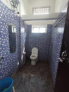 a bathroom with a toilet and blue tiled walls at Devagram Guest house in Dergaon +1 photo