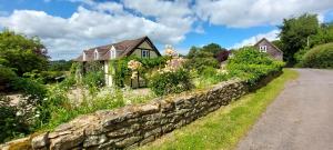 a house with a stone wall next to a road at Whitewells Farm Cottages - 7 exceptionally well appointed pet friendly barn conversions set in 10 acres of gardens, fields and woodland suitable from 2 to 24 people with breathtaking views towards the Malvern Hills, Herefordshire and Worcestershire in Mathon