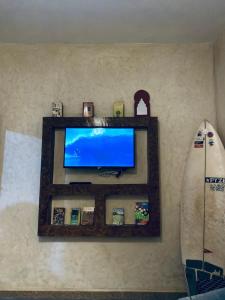 a television on a wall with a shelf and a surfboard at calm stay ouassane in Essaouira