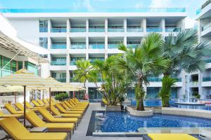 a hotel pool with yellow lounge chairs and palm trees at The Kee Resort & Spa in Patong Beach
