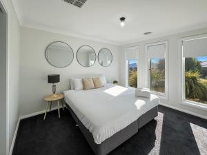 a white bedroom with a large bed and three mirrors at Paradise Stay in North Wagga