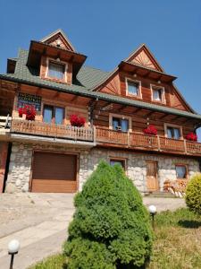 a large wooden house with red flowers on the balcony at Miodowa Chatka in Brzegi
