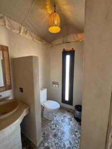 a bathroom with a toilet and a sink and a window at Desert Luxury Camp Erg Chigaga in El Gouera