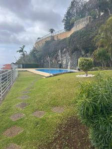 a grassy yard with a swimming pool next to a hill at Vista Calheta Apartment in Calheta