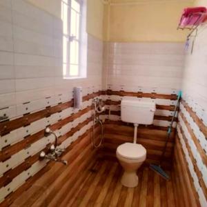 a bathroom with a toilet in a room with wooden floors at Za Homestay in Cherrapunji