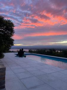 two people sitting next to a swimming pool at sunset at Complejo DOS LUNAS in San Roque