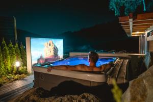 a man laying in a bath tub with a tv at Niebo Beskidu in Brenna
