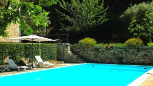 a blue swimming pool with two chairs and an umbrella at La Piccola Rocca in Cetona