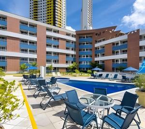 an outdoor swimming pool with chairs and tables in front of a building at Flat no Terrazzo perto do mar in Natal