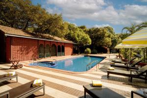 a swimming pool with benches and umbrellas next to a building at Chambers Mahabaleshwar, A Club Mahindra Associate Resort in Mahabaleshwar