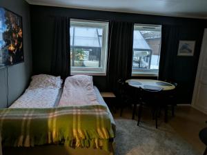 a bedroom with a bed and a table and two windows at E&E Apartment Junior in Svolvær