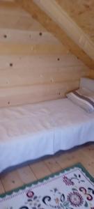 a bed in a wooden attic with a rug on the floor at Vikendica strane in Mateševo