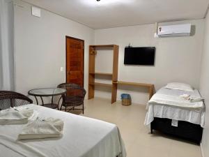 a room with two beds and a table and a tv at Villa Manoá in São Miguel dos Milagres