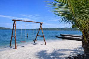 an empty swing on a beach next to the water at Akwaba Lodge Island Boutique Hotel in The Gap