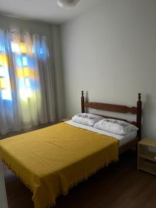 a bedroom with a bed with a yellow bedspread and a window at Hospedagem Casa de Déo in Domingos Martins