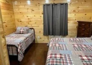 two beds in a room with wooden walls and a window at Blue Cozy Cottage in Oneida