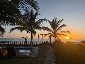a sunset at a resort with palm trees and the ocean at Vila Sereia Caraiva in Caraíva