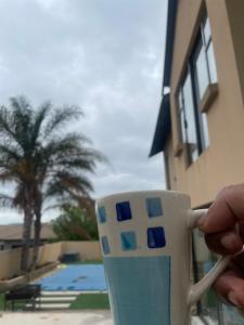 eine Person, die eine Kaffeetasse vor einem Pool hält in der Unterkunft Madlabeezy in Kempton Park + 7 Fotos
