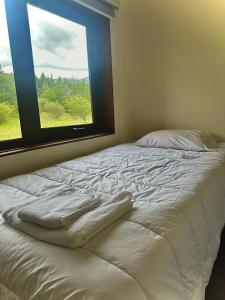 a white bed with a window in a bedroom at Cabañas Raíces de la Patagonia in Coihaique +1 photo
