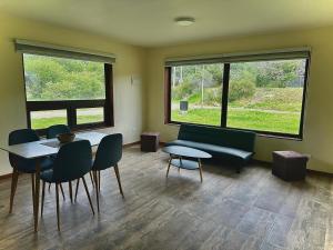 a room with a table and chairs and two windows at Cabañas Raíces de la Patagonia in Coihaique