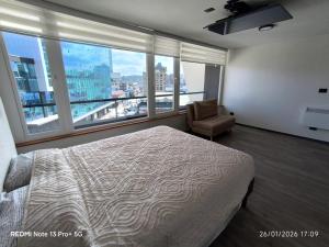 a bedroom with a bed and a chair and windows at Departamento Piso 6 in Puerto Montt