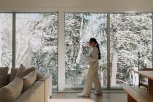 a woman walking in a living room looking out of a window at Private Nordic Spa Retreat - Mont-Tremblant in Lac-Superieur