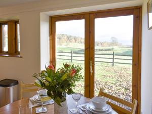 a table with a vase of flowers on it with a window at Quarry Cottage in Penrith