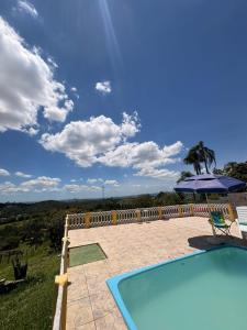 a swimming pool with an umbrella and a palm tree at Chácara Pagliai e Bueno in Suzano