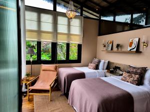 a room with two beds and a chair and windows at The Little Hill Suite in Munduk