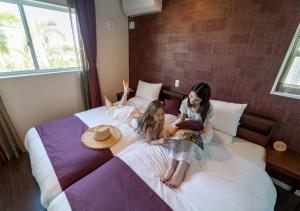two little girls are sitting on a bed at BEVERLY HILLS VILLA Miyakojima Resort in Miyako-jima