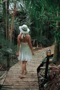 a girl in a white dress and hat walking down a wooden path at Amore On Buderim Rainforest Cabins in Buderim +3 photos