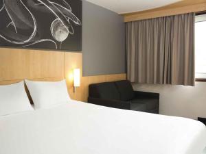 a hotel room with a bed and a chair at ibis 3 Lacs Neuchâtel in Thielle