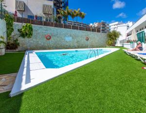 una piscina con césped junto a un edificio en Tagoror Beach Apartments - Adults Only en Playa del Inglés