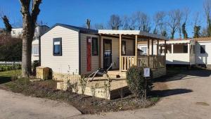 a small white house with a porch and a tree at Camping Vauban in Bergues