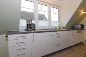 a kitchen with white cabinets and two windows at Wodan, Whg 2 in Tinnum
