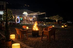 a fire pit with chairs and a house with christmas lights at Forest Nest Farm Stay in Rājpur