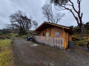 a small wooden cabin with a fence in a field at Eas Lodge in Tobermory
