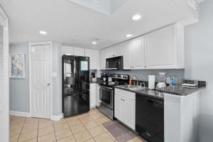 a kitchen with a black refrigerator and white cabinets at Oceanside Escape Condo w/ Ocean Views + Pools in Myrtle Beach