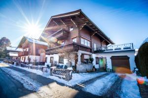 a house in the snow with the sun behind it at Pension Kuntschner in Mittersill