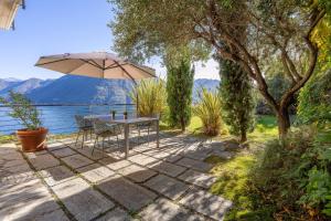a patio with an umbrella and a table and chairs at Residence degli Oleandri APP A1 in Argegno