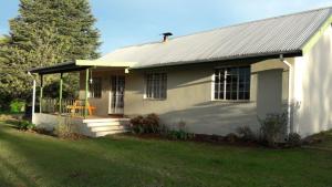 a white house with a porch and a yard at Under The Oak in Underberg